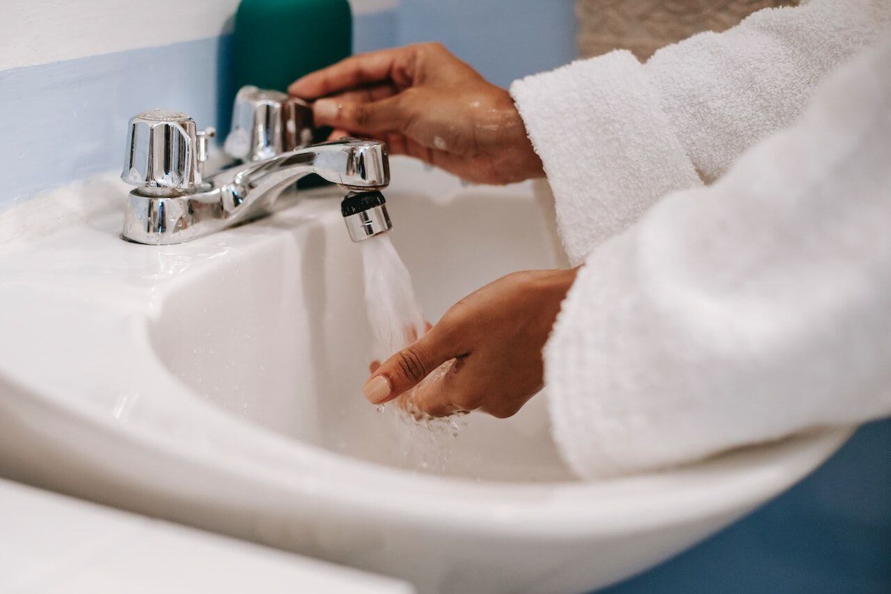 woman's hands under high hot water pressure faucet
