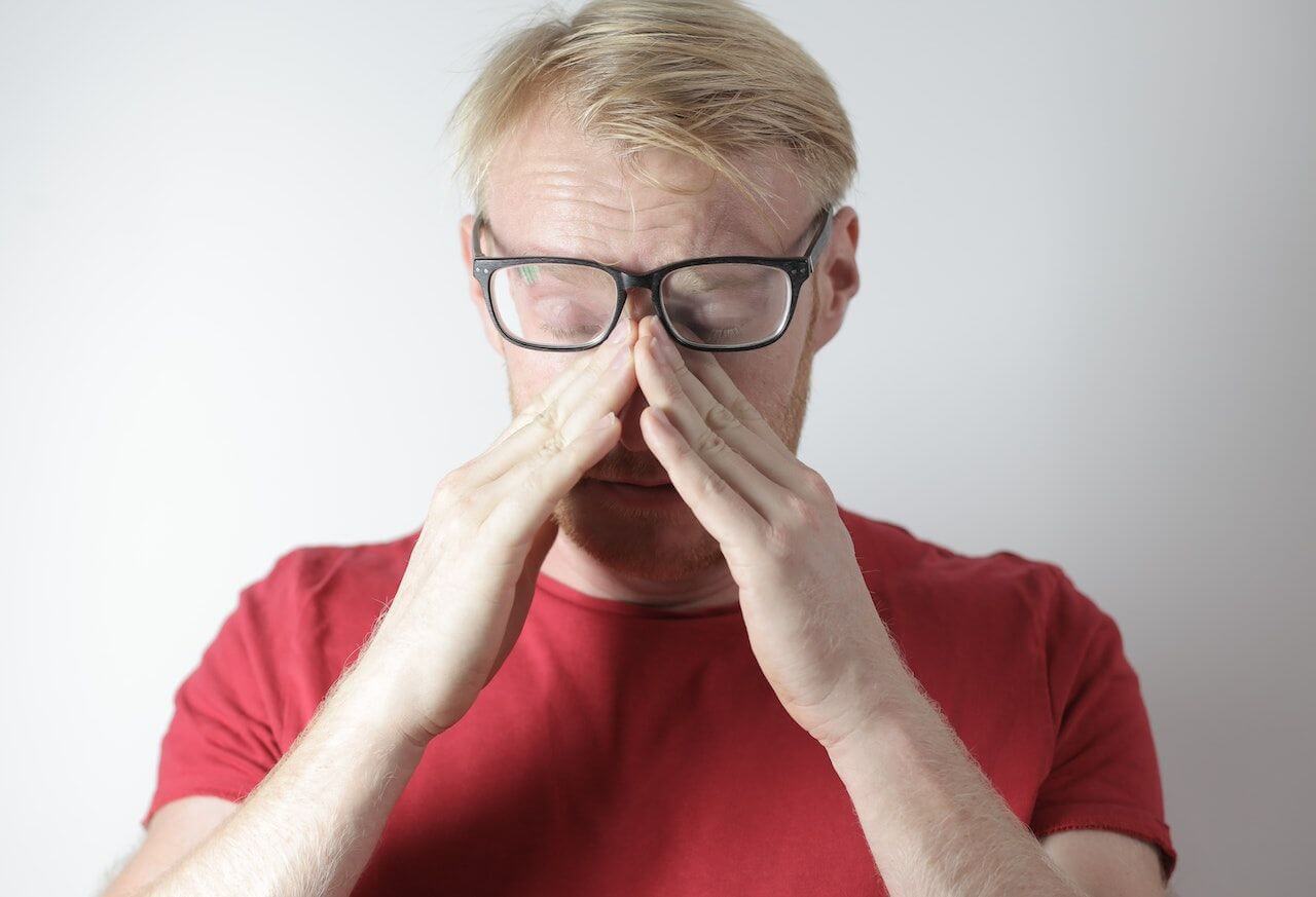Man in red shirt and glasses covering his nose